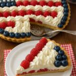 American Flag Fruit Pizza decorated with fresh raspberries, blueberries, and whipped cream in a patriotic pattern.