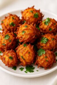 Crispy golden air-fryer onion bhajis garnished with fresh cilantro, served on a white plate.