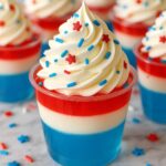 Festive 4th of July Jello Shots layered with blue, white, and red jello, topped with creamy whipped topping and patriotic sprinkles.