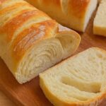 Close-up of freshly baked fluffy French bread with a soft, airy interior and golden crust, sliced on a wooden board.