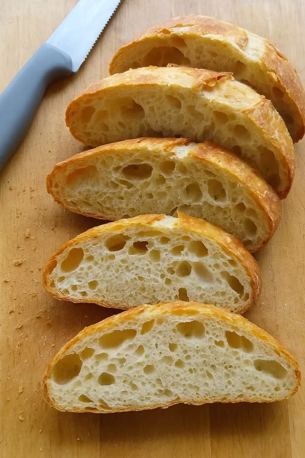 Close-up of freshly sliced no-knead bread with a golden crust and airy, soft interior on a wooden cutting board.