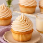 Snickerdoodle cupcakes topped with cinnamon buttercream frosting on a ceramic plate with a soft napkin.