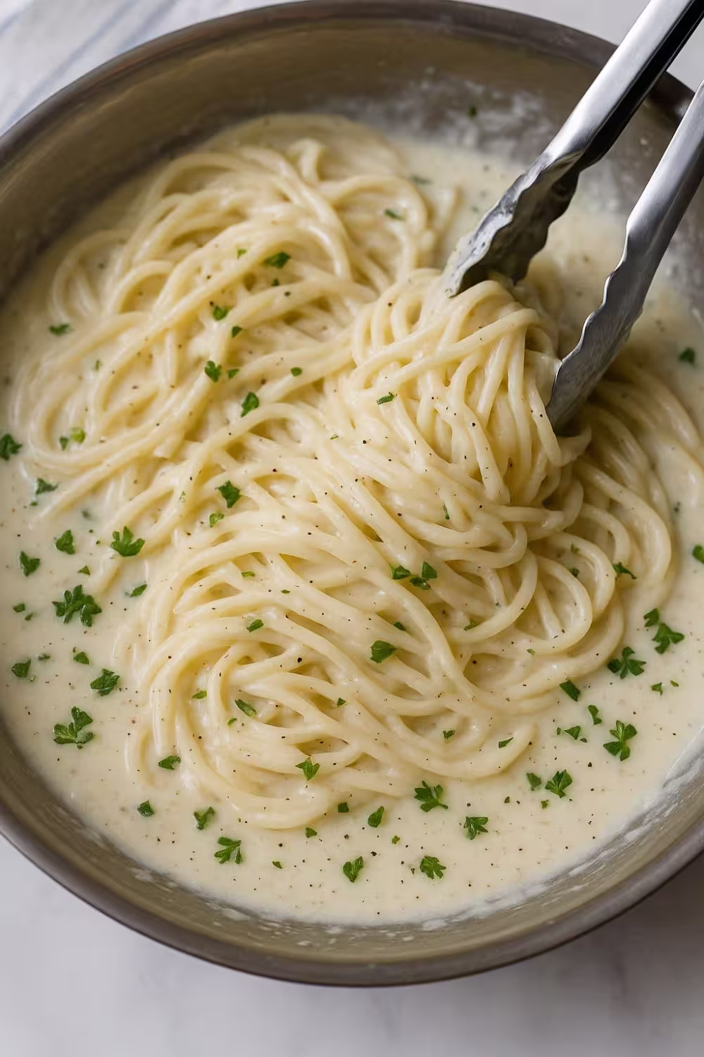 Creamy garlic parmesan pasta tossed with herbs in a stainless steel pan.