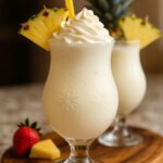 A creamy Pina Colada Milkshake topped with whipped cream, garnished with a fresh pineapple slice, served in a decorative glass with a yellow straw.