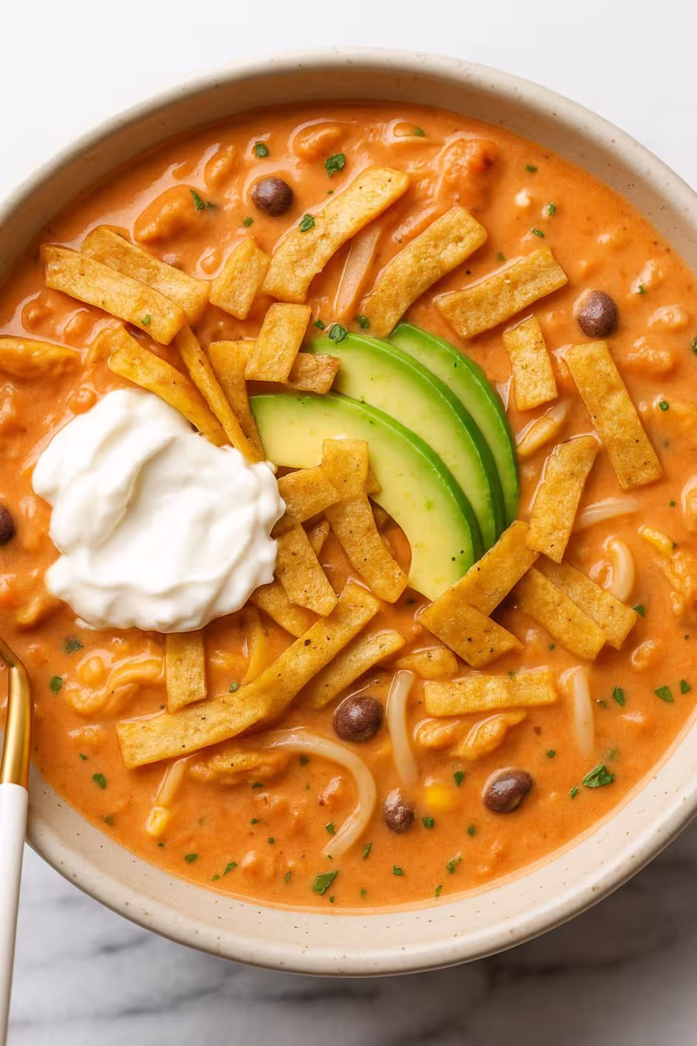 Creamy Chicken Tortilla Soup topped with avocado slices, crispy tortilla strips, and a dollop of sour cream.