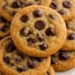Stack of golden brown chocolate chip cookies with gooey chocolate chips on a white plate.