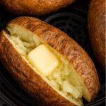 Close-up of a crispy air fryer baked potato split open with a pat of butter melting inside