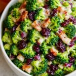 Creamy broccoli salad with bacon, cranberries, red onions, and almonds in a white bowl.