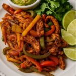 A plate of vibrant air fryer chicken fajitas with colorful bell peppers, served with guacamole, fresh cilantro, and lime wedges.