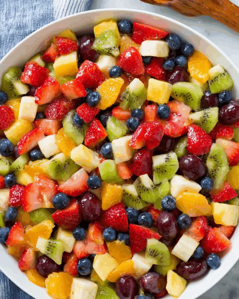 Honey Lime Rainbow Fruit Salad with strawberries, kiwi, bananas, blueberries, grapes, oranges, and pineapple in a white bowl.