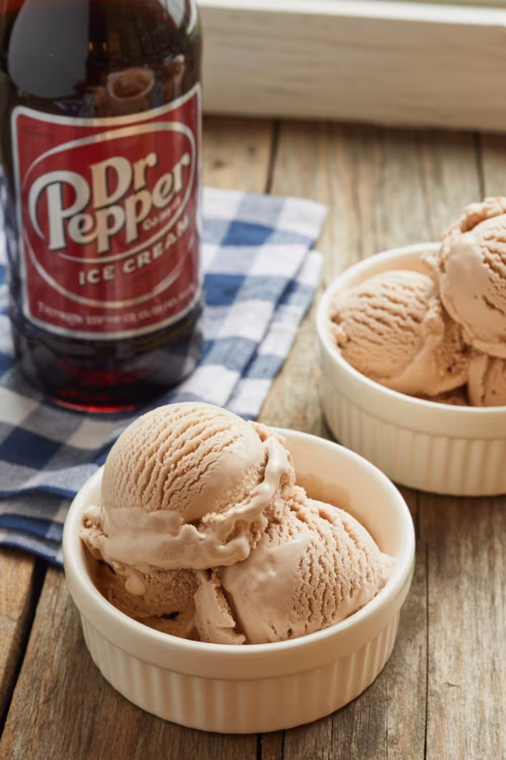 Creamy homemade Dr Pepper ice cream served in white bowls beside a soda bottle