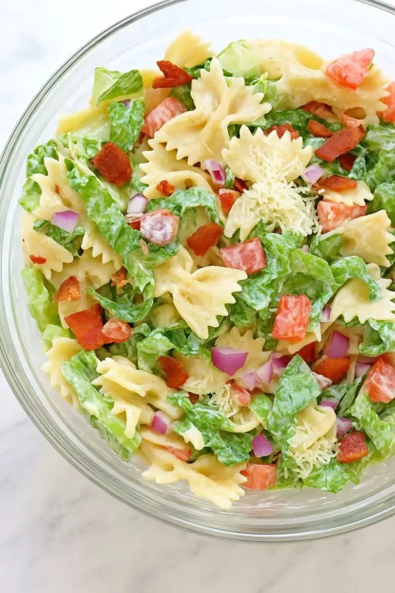 A colorful bowl of BLT pasta salad featuring bowtie pasta, crispy bacon, fresh lettuce, diced tomatoes, red onions, and creamy dressing.
