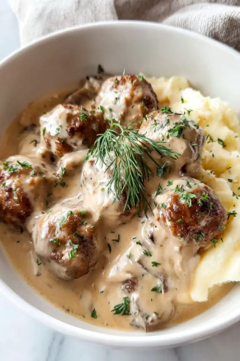 A bowl of creamy Swedish meatballs served over fluffy mashed potatoes, garnished with fresh parsley.