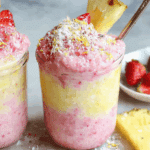 Anti-Inflammatory Pineapple Smoothie layered with pink and yellow swirls, topped with coconut, strawberry slices, and a pineapple wedge.