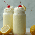Frozen Whipped Lemonade in glass jars topped with whipped cream, cherries, and lemon slices.