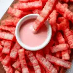 Healthy Watermelon Fries served with pink yogurt dip, arranged on a wooden board.