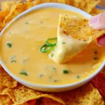Costa Vida Queso Recipe served in a bowl with tortilla chips, with a chip dipped into the creamy cheese sauce.