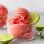 Glass bowl filled with 2-ingredient watermelon sorbet, garnished with a slice of lime, and surrounded by fresh lime halves.