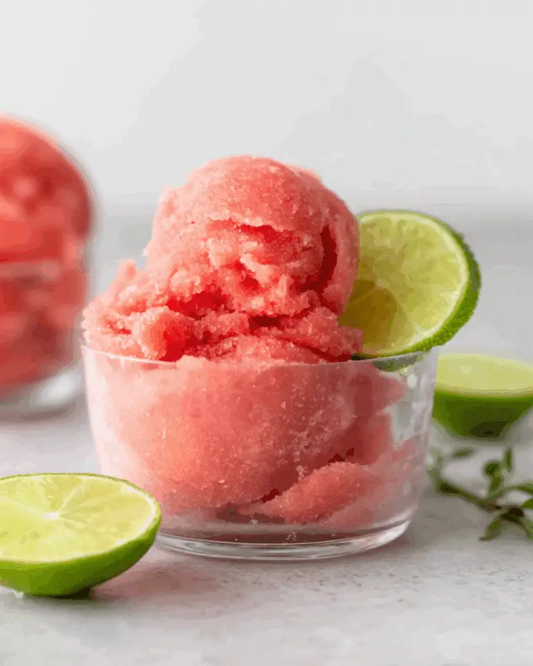 Glass bowl filled with 2-ingredient watermelon sorbet, garnished with a slice of lime, and surrounded by fresh lime halves.