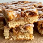 Apple cinnamon sheet cake slices stacked on a wooden surface, drizzled with icing and filled with gooey cinnamon-apple layers.