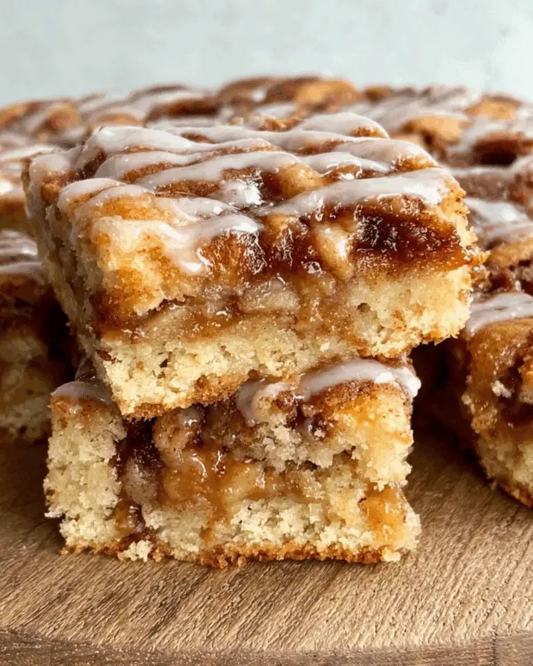 Apple cinnamon sheet cake slices stacked on a wooden surface, drizzled with icing and filled with gooey cinnamon-apple layers.