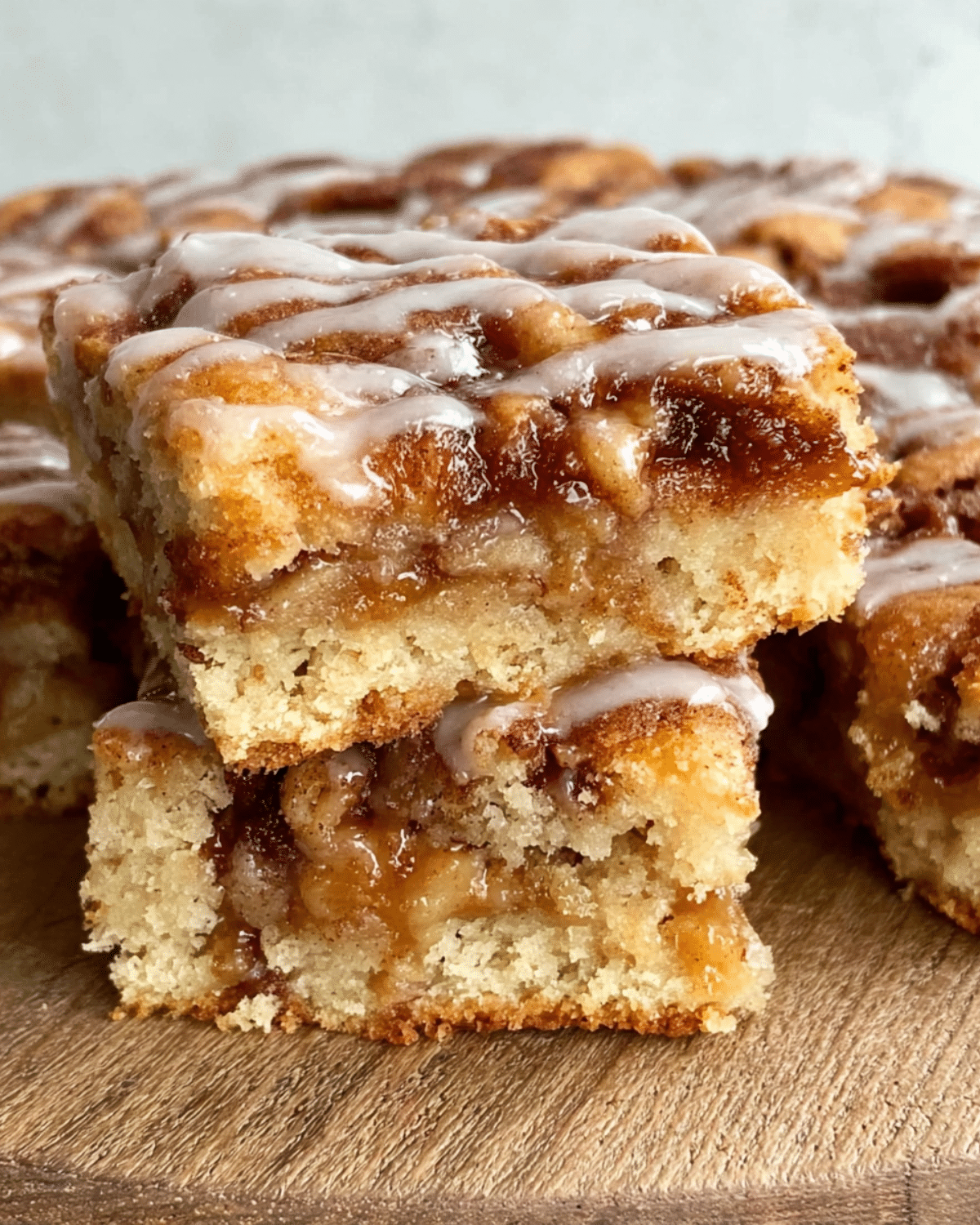 Apple cinnamon sheet cake slices stacked on a wooden surface, drizzled with icing and filled with gooey cinnamon-apple layers.