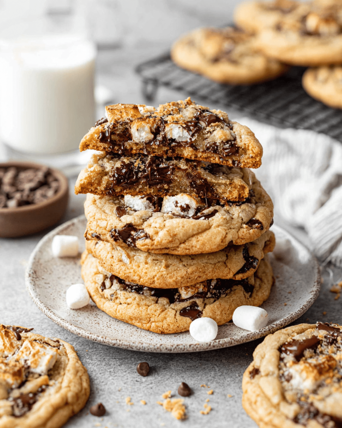 Stack of gooey s'mores cookies with melted chocolate, toasted marshmallows, and graham cracker crumbs, served with a glass of milk.