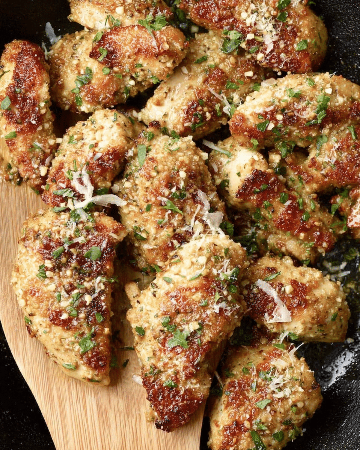 Crispy Blackstone garlic parmesan chicken pieces garnished with fresh parsley and grated parmesan cheese on a wooden spatula.