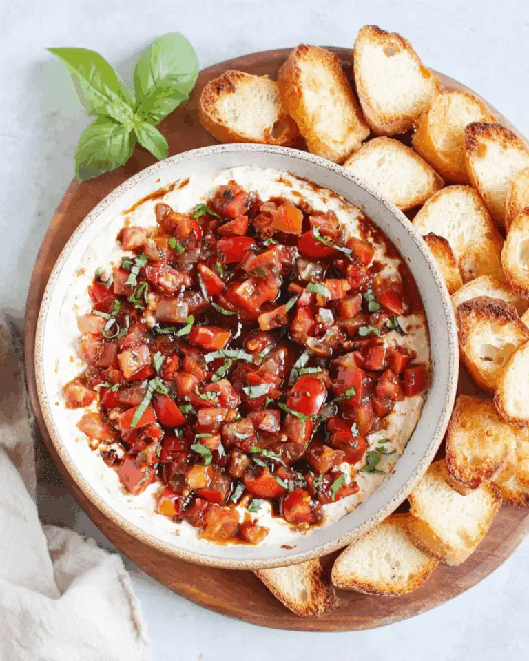 Bruschetta dip topped with diced tomatoes, basil, and balsamic glaze, served with toasted baguette slices on a wooden platter.