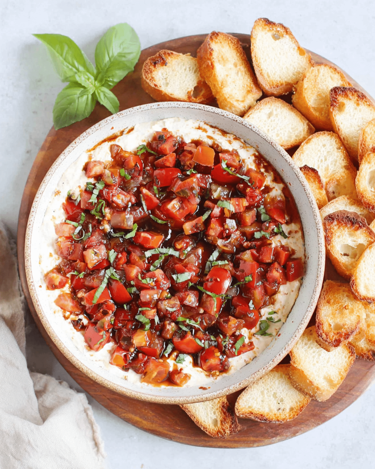 Bruschetta dip topped with diced tomatoes, basil, and balsamic glaze, served with toasted baguette slices on a wooden platter.