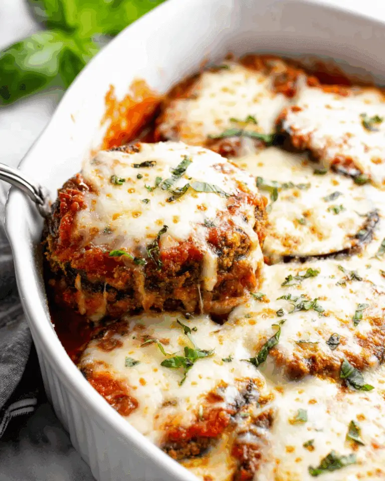 Baked Cheesy Oven Eggplant Parmesan in a white dish, topped with melted mozzarella, tomato sauce, and fresh basil.