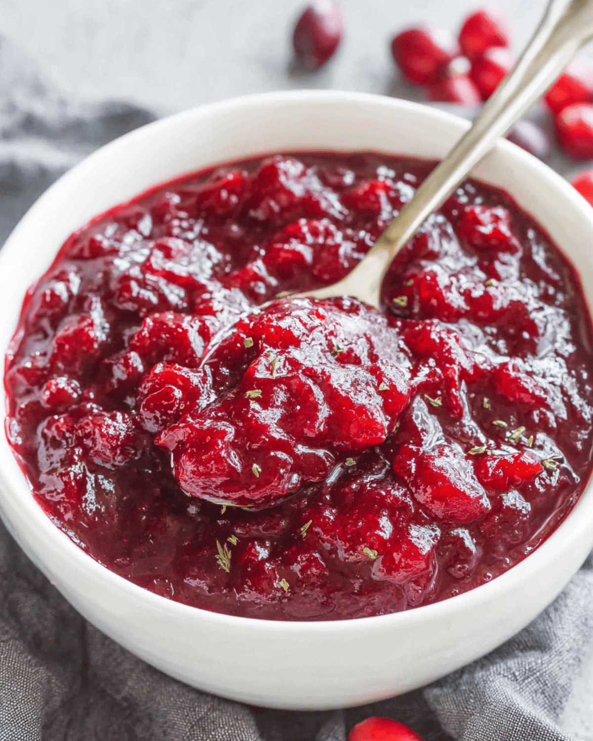 Classic homemade cranberry sauce in a white bowl with a spoon, showing a thick and chunky texture.