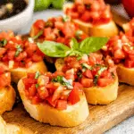Classic Italian bruschetta topped with diced tomatoes and fresh basil on toasted baguette slices, served on a wooden board.