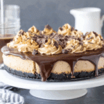 Coffee Cheesecake topped with chocolate ganache, coffee whipped cream swirls, and chocolate chunks on a white cake stand.