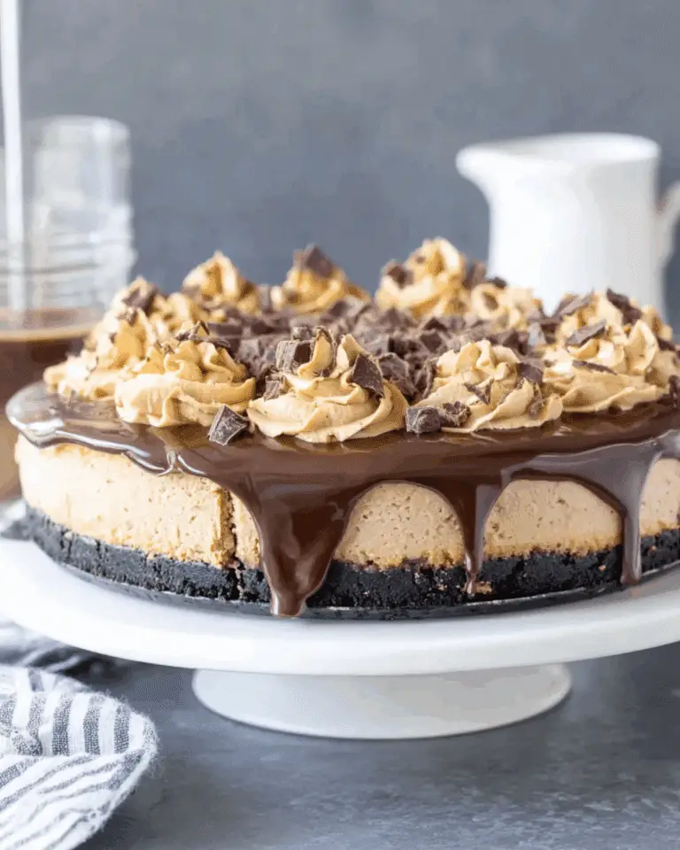 Coffee Cheesecake topped with chocolate ganache, coffee whipped cream swirls, and chocolate chunks on a white cake stand.