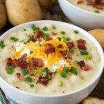 Cozy Fall Potato Soup topped with shredded cheddar cheese, crispy bacon, sour cream, and chopped green onions in a white bowl.