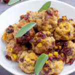 A white bowl filled with cranberry turkey stuffing balls, garnished with fresh sage leaves and dried cranberries.