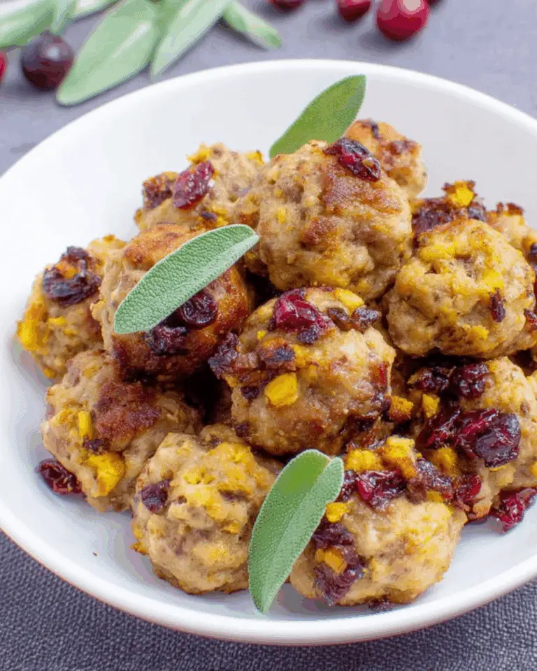 A white bowl filled with cranberry turkey stuffing balls, garnished with fresh sage leaves and dried cranberries.