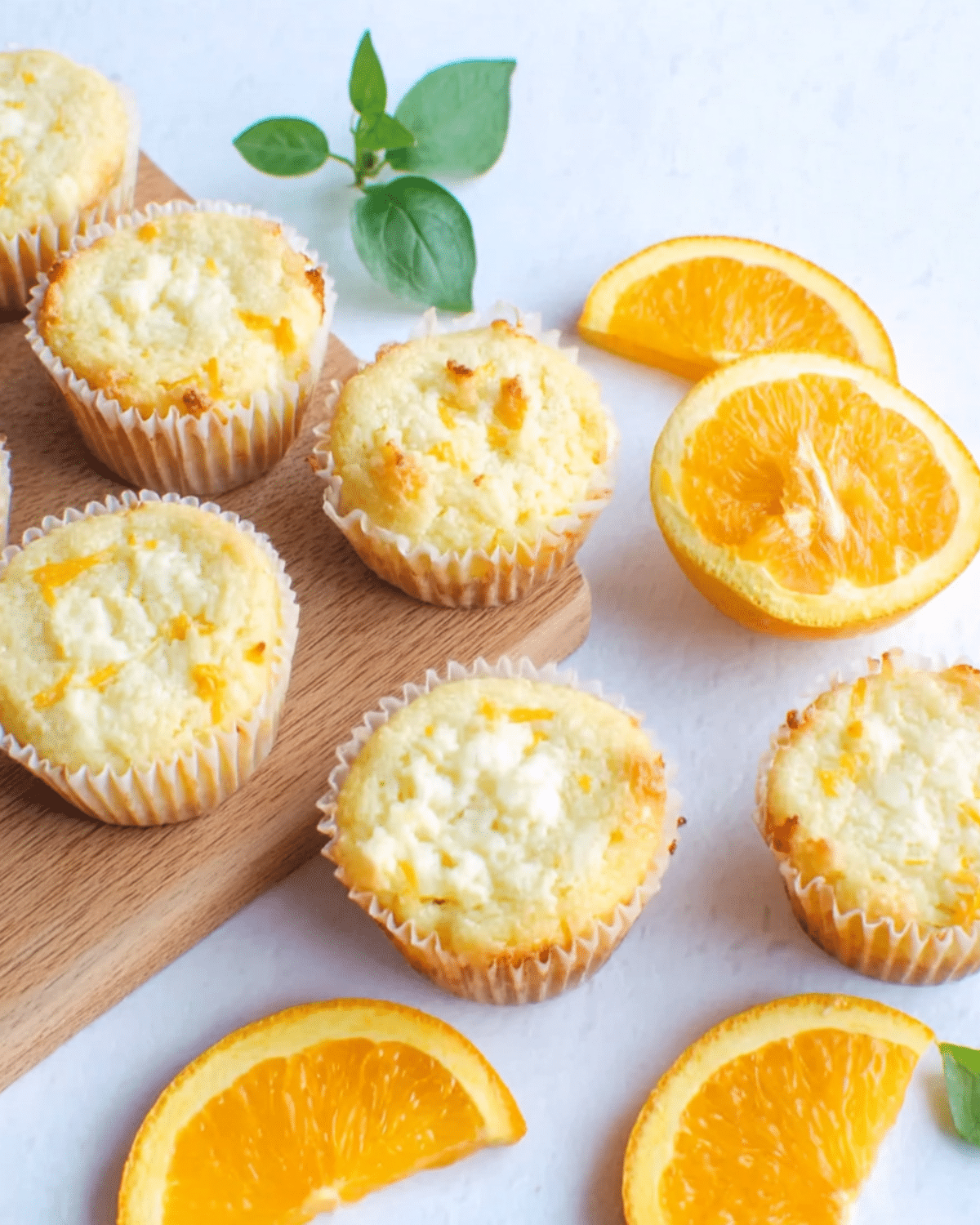 Creamy orange muffins with golden tops, surrounded by fresh orange slices and green leaves.