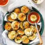 Crispy baked zucchini slices in a bowl with dipping sauces on the side.