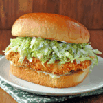 Crispy chicken Caesar sandwich with breaded chicken, shredded romaine lettuce, Caesar dressing, and a toasted bun on a white plate.