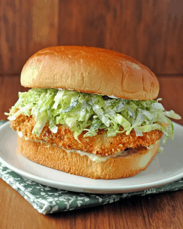 Crispy chicken Caesar sandwich with breaded chicken, shredded romaine lettuce, Caesar dressing, and a toasted bun on a white plate.