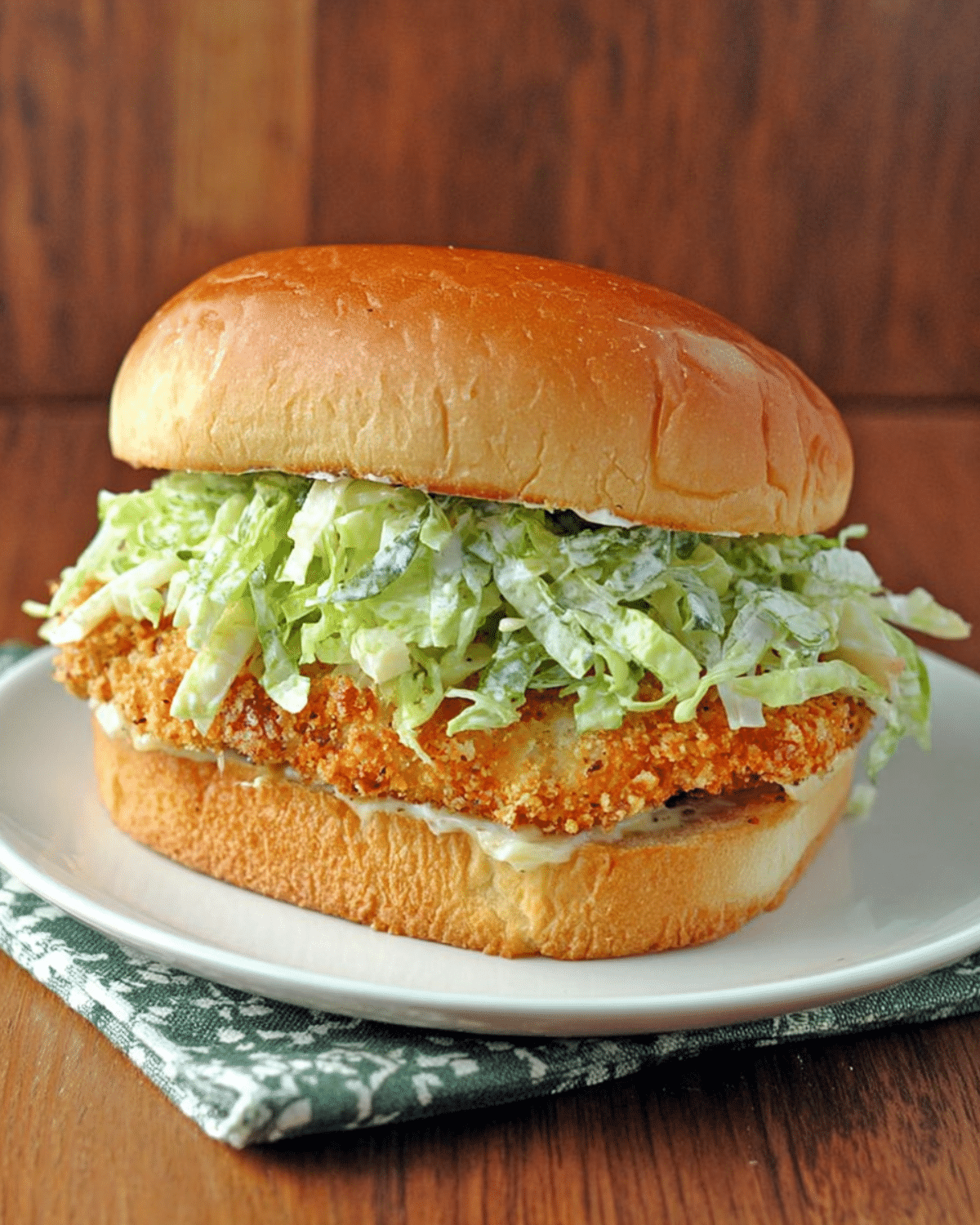 Crispy chicken Caesar sandwich with breaded chicken, shredded romaine lettuce, Caesar dressing, and a toasted bun on a white plate.