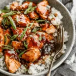 Crock Pot Bourbon Chicken served over white rice and garnished with sliced green onions and sesame seeds.