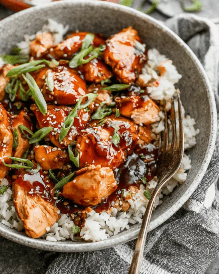 Crock Pot Bourbon Chicken served over white rice and garnished with sliced green onions and sesame seeds.