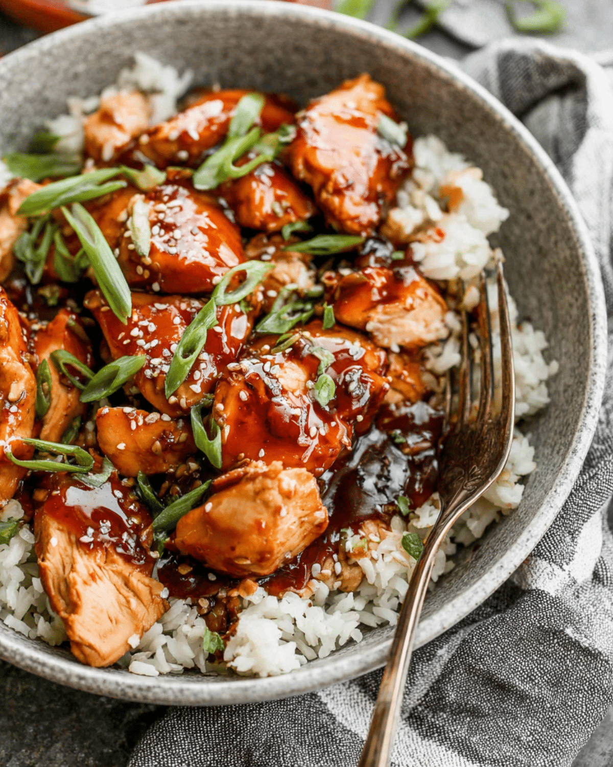 Crock Pot Bourbon Chicken served over white rice and garnished with sliced green onions and sesame seeds.