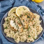 Plate of crock pot chicken and rice recipe, featuring sliced grilled chicken breast over a bed of seasoned rice, garnished with lemon slices and fresh herbs.