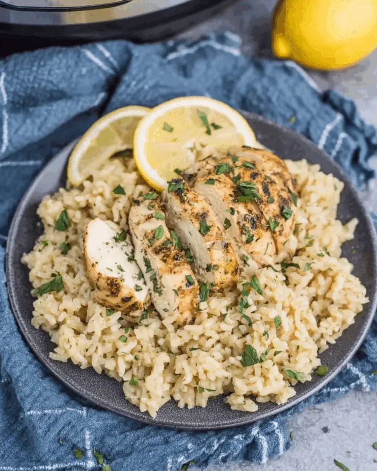 Plate of crock pot chicken and rice recipe, featuring sliced grilled chicken breast over a bed of seasoned rice, garnished with lemon slices and fresh herbs.