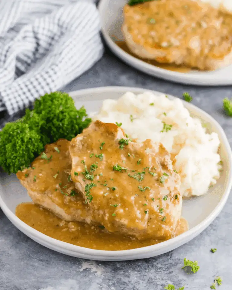 Plate of crock pot pork chops smothered in gravy, served with mashed potatoes and a side of parsley garnish.