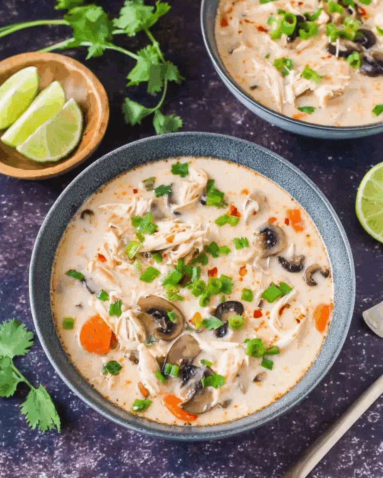 Bowl of crockpot Thai coconut chicken soup filled with shredded chicken, mushrooms, carrots, and green onions in a creamy coconut broth.